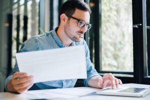 man holding pen and paper typing on laptop