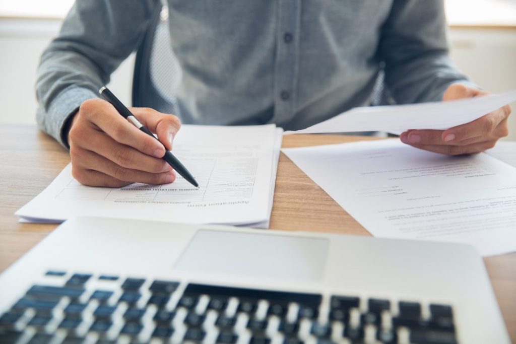 man with paper and laptop on desk holding a pen