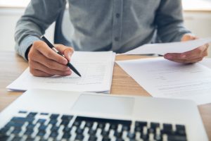man with paper and laptop on desk holding a pen